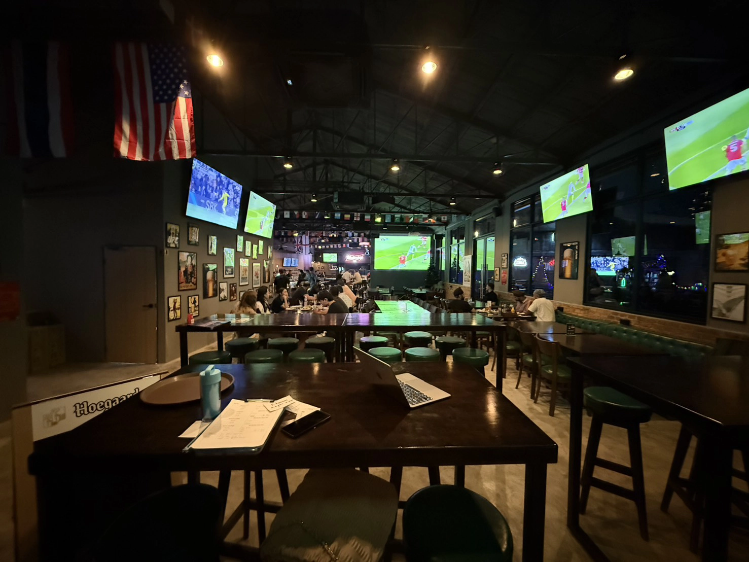 Wide interior view of Upper Deck Sports Bar featuring high wooden tables, green bar stools, and multiple wall-mounted HD screens broadcasting live sports matches.